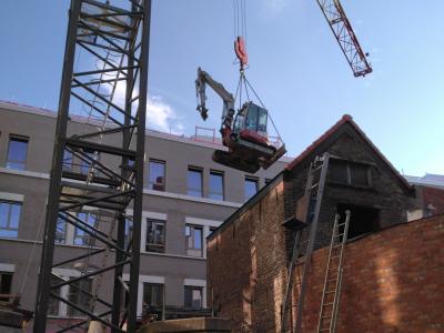 GLK minigraver hoog in de lucht met torenkraan om over hoog gebouw te plaatsen